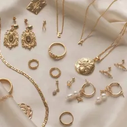 Gold earrings, rings, chains and pendants arranged on a cream surface.