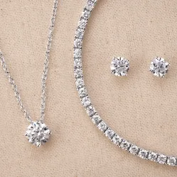 A diamond necklace and matching stud earrings on a linen background.